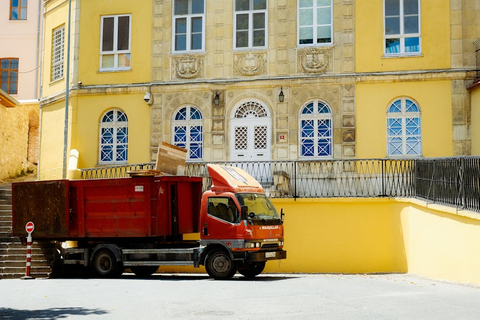 Photograph showing a professional house removal team's loading process inside a property, where a mover is carefully carrying a cardboard box wrapped in plastic film towards a doorway leading to a spa