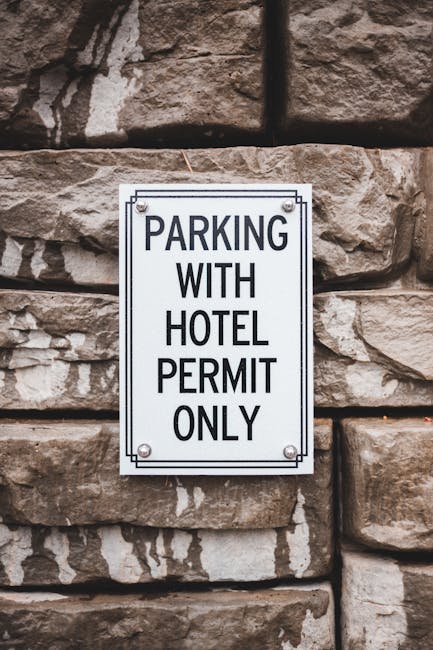 A blue parking sign with a white letter 'P' and a wheelchair symbol, indicating accessible parking, mounted on a silver metal post against a dark grey textured wall. The shadow of the sign is cast on